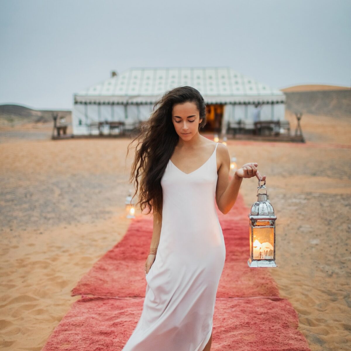 Beautiful oriental young brunette woman in white dress walking near luxury glamping tent camp